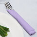 A fork and knife wrapped in a Luscious Lavender purple napkin next to a plate of green beans.