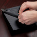 A person's hands wrapping silverware in a black velvet Creative Converting luncheon napkin.