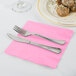 A fork and knife on a pink napkin.