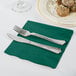 A knife and fork on a Hunter Green Creative Converting napkin next to a plate of food.