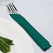 A fork and knife wrapped in a hunter green Creative Converting luncheon napkin on a plate.