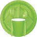 A Fresh Lime Green Creative Converting paper napkin with green plastic plates and cups with forks and spoons.