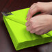 A person wrapping a Creative Converting Fresh Lime Green napkin around a fork and knife.