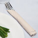 A fork and knife wrapped in an ivory Creative Converting luncheon napkin next to a plate of green beans.