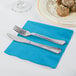 A silver fork and knife on a turquoise blue Creative Converting luncheon napkin.