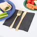 A black Creative Converting luncheon napkin with a fork and knife next to a plate of food.