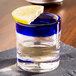 A Libbey shot glass with a cobalt blue rim filled with liquid and a lemon wedge on top.
