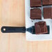 A brownie on a square plate being lifted with a Tablecraft FirmGrip slotted mini turner.