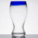 A Libbey pilsner glass with a cobalt blue rim on a table.