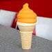 A close up of an ice cream cone with Phillips Butterscotch Shell Coating with orange swirls on top.
