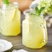 Two Acopa Rustic Charm mason jars filled with lemonade and mint, each with a lemon and leaf on top.