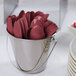 A bucket filled with burgundy plastic spoons and forks.