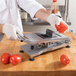 A person using a Nemco Roma Tomato Slicer to slice tomatoes on a counter.