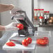A person using a Nemco Roma tomato slicer to slice tomatoes on a cutting board.