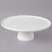A 10 Strawberry Street Whittier white porcelain footed cake stand holding a round white plate with a white cake on it.