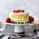 A white cake on a 10 Strawberry Street white porcelain cake stand with strawberries and blueberries on top.
