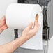 A person holding a Lavex White Hardwound Paper Towel roll in front of a dispenser.