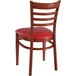 A Lancaster Table & Seating Spartan Series metal ladder back chair with mahogany wood grain finish and red vinyl seat.