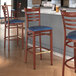 Three Lancaster Table & Seating metal ladder back bar stools with navy vinyl seats in a restaurant.