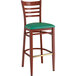 A Lancaster Table & Seating metal ladder back bar stool with mahogany wood grain finish and green vinyl seat.