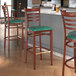 A set of three Lancaster Table & Seating metal ladder back bar stools with mahogany wood grain finish and green vinyl seats.