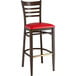 A Lancaster Table & Seating Spartan Series metal ladder back bar stool with red vinyl seat and dark walnut wood grain finish.
