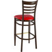 A metal ladder back restaurant bar stool with a red vinyl seat.