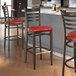 A Lancaster Table & Seating metal ladder back bar stool with a dark walnut wood grain finish and red vinyl seat.