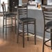A group of Lancaster Table & Seating metal ladder back bar stools with black vinyl seats next to a counter.