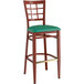 A Lancaster Table & Seating metal window back bar stool with a mahogany wood grain finish and green vinyl seat.