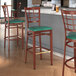A group of Lancaster Table & Seating Spartan Series bar stools with green vinyl seats and mahogany wood grain finishes at a bar.