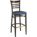 A Lancaster Table & Seating Spartan Series metal ladder back bar stool with a dark walnut wood grain finish and navy vinyl seat.