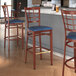 A Lancaster Table & Seating bar stool with a navy vinyl seat and mahogany wood grain finish.