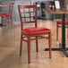 A Lancaster Table & Seating Spartan Series metal chair with mahogany wood grain finish and red vinyl seat.