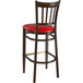 A Lancaster Table & Seating metal slat back bar stool with a dark walnut wood grain finish and red vinyl seat.