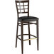 A Lancaster Table & Seating Spartan Series metal bar stool with dark walnut wood grain finish and black vinyl seat.