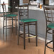 A Lancaster Table & Seating Spartan Series metal bar stool with a green vinyl seat.