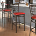 A Lancaster Table & Seating Spartan Series metal bar stool with a dark walnut wood grain finish and red vinyl seat.