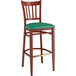 A Lancaster Table & Seating metal slat back bar stool with mahogany wood grain finish and a green vinyl seat.