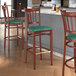 A Lancaster Table & Seating Spartan Series bar stool with a green vinyl seat on a wood surface.