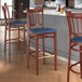 A Lancaster Table & Seating bar stool with a navy vinyl seat and mahogany wood grain finish.