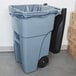 A Rubbermaid grey wheeled rectangular trash can with black lid and handle.
