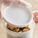 A hand holding a white plastic round deli lid over a container with food inside.