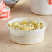 A bowl of potato salad in a white and red Choice deli container on a counter.