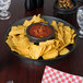 A black round deli server filled with chips and a bowl of salsa on a table.