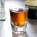 An Anchor Hocking fluted shot glass with a shot of brown liquid in it.