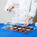 A chef holding a Cal-Mil clear rectangular bakery tray cover over a tray of brownies.