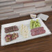 An American Metalcraft antique white melamine platter with cheese, grapes, and meat on a table.