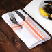 An orange and white striped Snap Drape cloth napkin with a fork and knife on a plate of mussels.