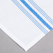A close up of a white and blue Snap Drape Softweave Bistro striped cloth napkin.